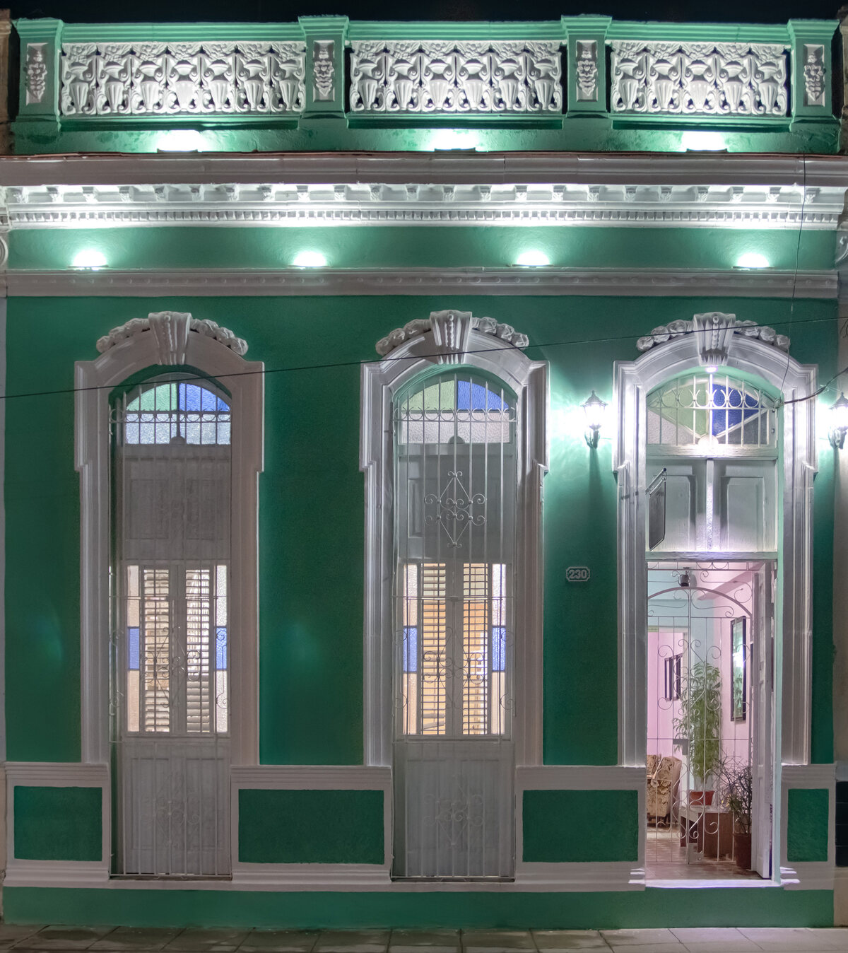 Fachada verde esmeralda del Hostal Familiar Rivalta iluminada de noche, con molduras coloniales blancas y el número 230